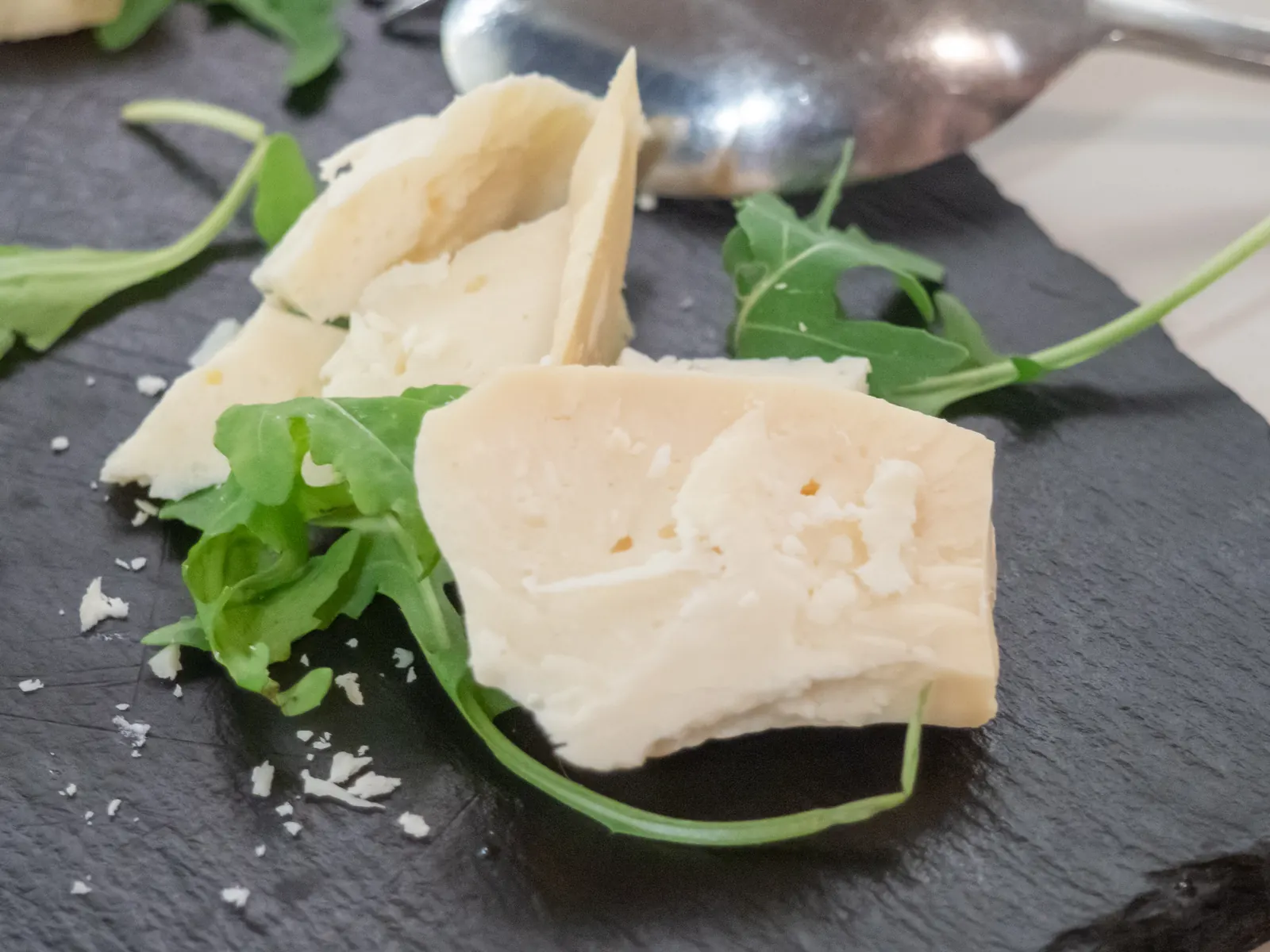 Pieces of Arseniko Naxou, a local Naxos cheese, on a slate board with rocket leaves and a spoon