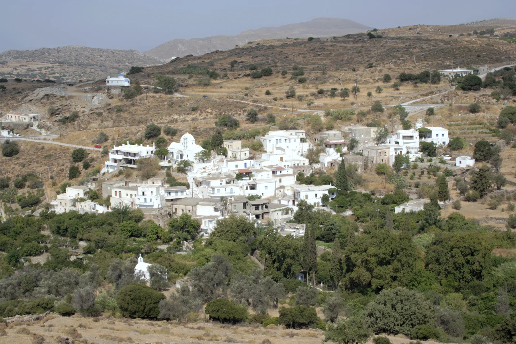 White houses and small chapels of the village of Mesi Potamia scattered across dry, olive-green hills on Naxos